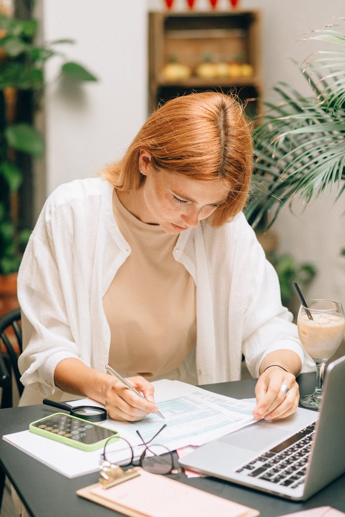 our-services-1 Woman analyzing financial documents using laptop and calculator indoors.